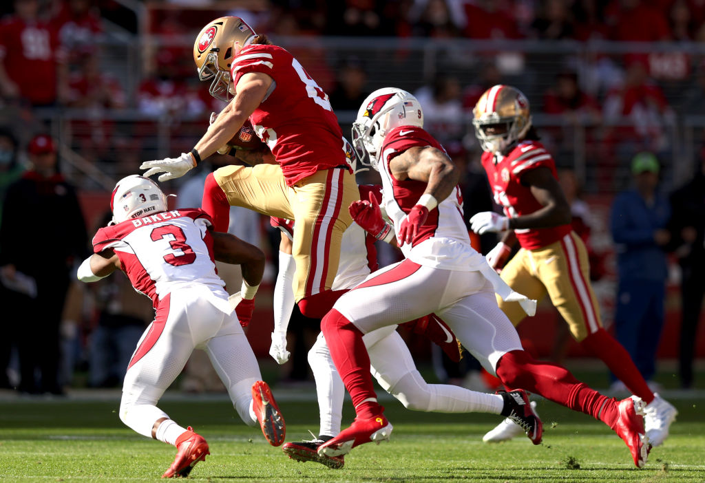 George Kittle #85 of the San Francisco 49ers leaps over Budda Baker #3 of the Arizona Cardinals but...