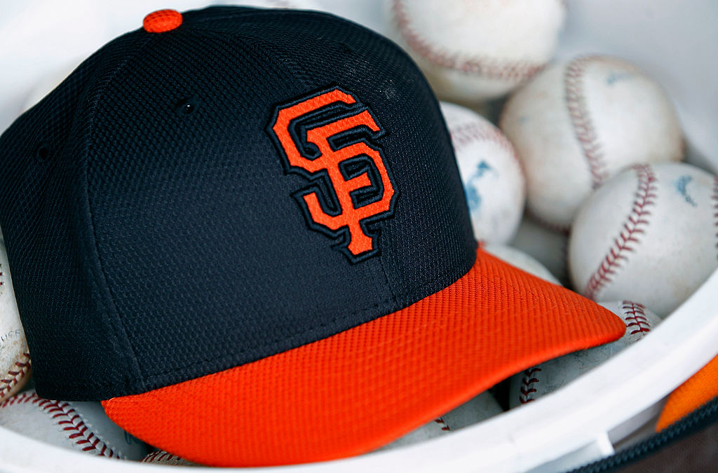 A San Francisco Giants hat sits in a bucket of baseballs during a Cactus League game between the Gi...