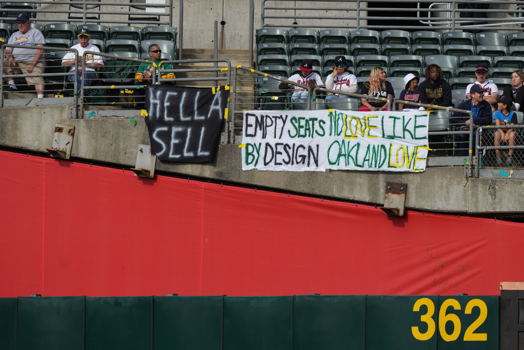 Fans sit behind signs referencing plans for the Oakland Athletics to move to Las Vegas during a gam...