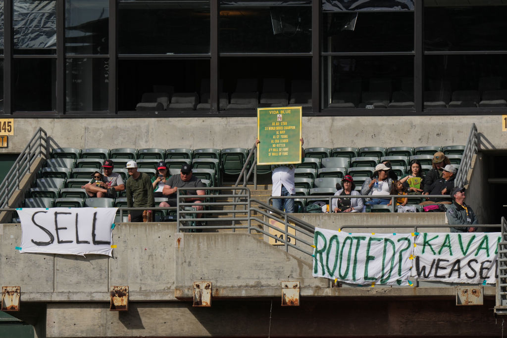 Fans sit behind signs referencing plans for the Oakland A's to move to Las Vegas during a game agai...