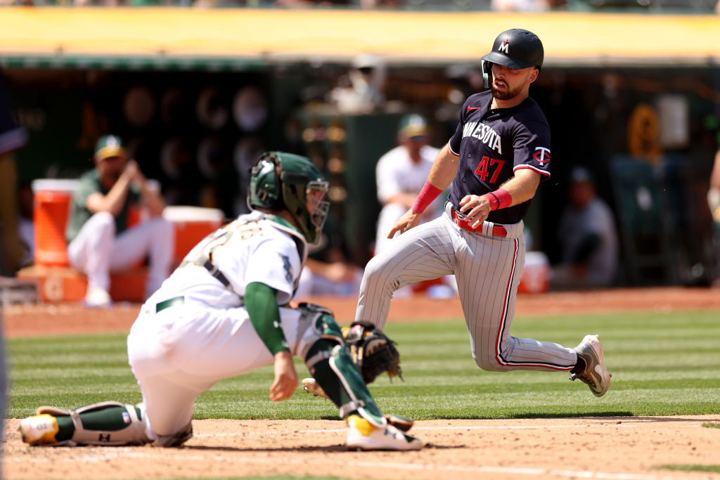 Edouard Julien #47 of the Minnesota Twins slides past Shea Langeliers #23 of the Oakland Athletics ...