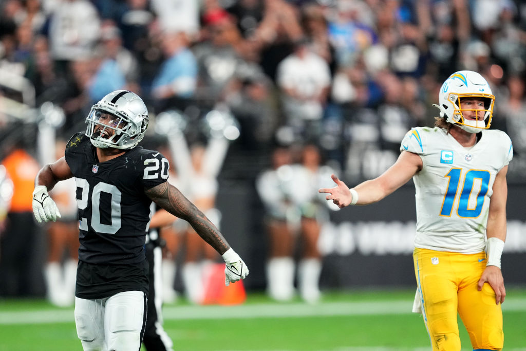 Justin Herbert #10 of the Los Angeles Chargers and Isaiah Pola-Mao #20 of the Las Vegas Raiders rea...