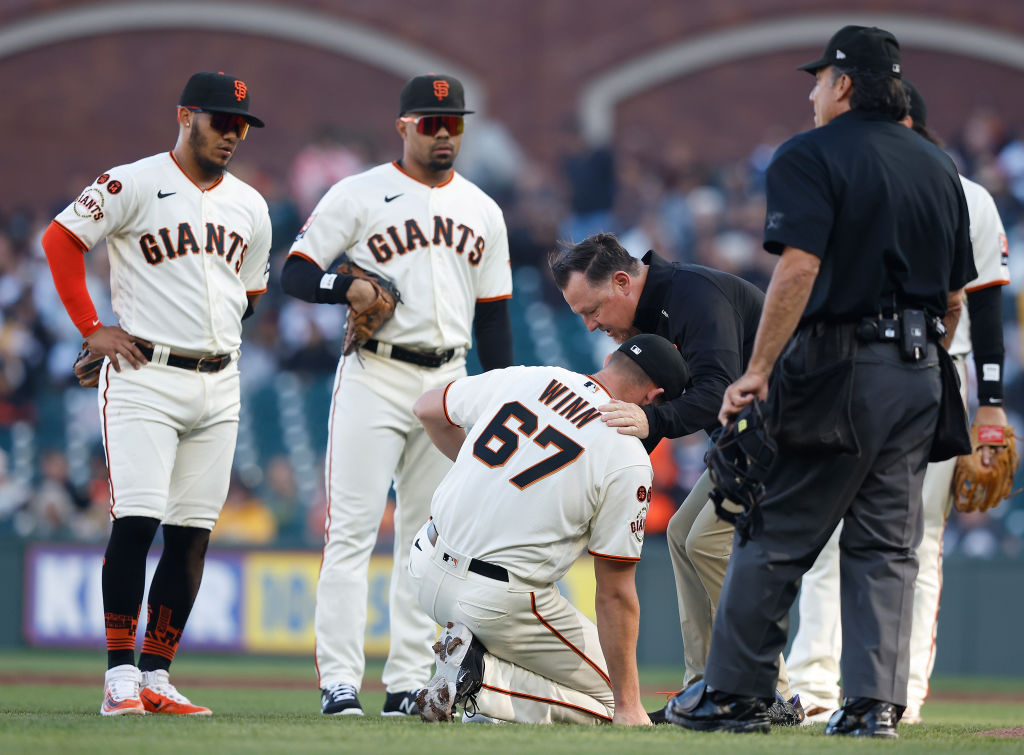 Pitcher Keaton Winn #67 of the San Francisco Giants is assisted by trainer Dave Groeschner after be...