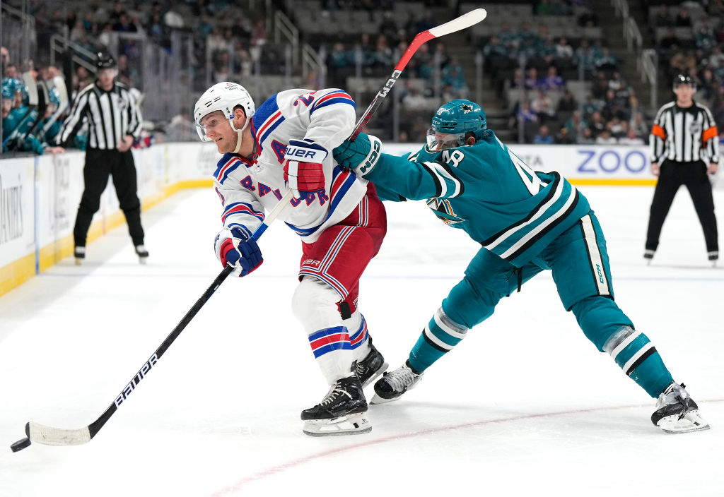 Adam Fox #23 of the New York Rangers gets cross-checked by Tomas Hertl #48 of the San Jose Sharks d...