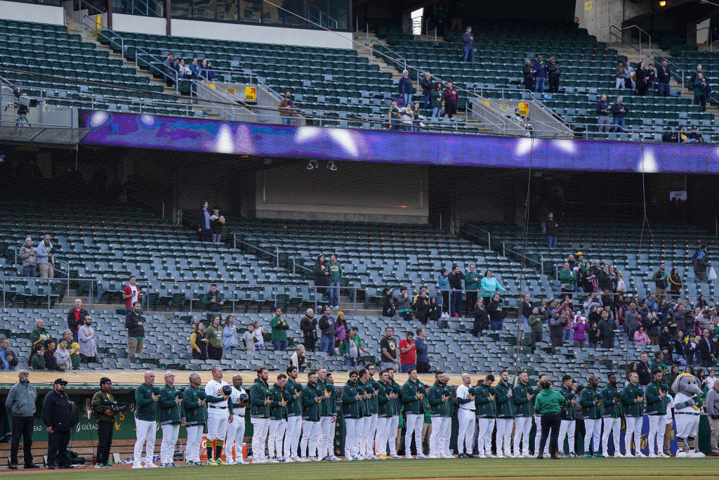 Oakland Athletics players observe the national anthem in front of mostly empty seats before playing...